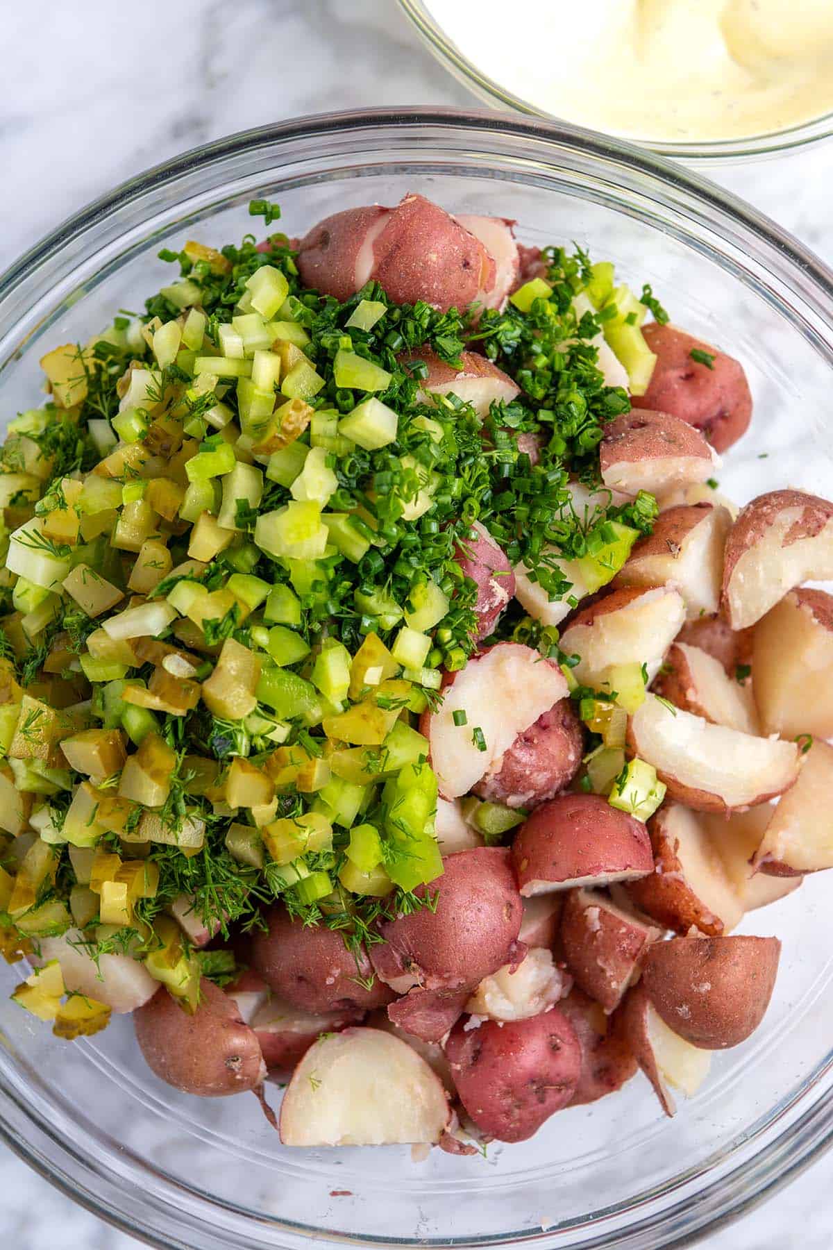 Making red potato salad -- Mixing bowl with red potatoes, herbs, chopped celery, and chopped pickles.