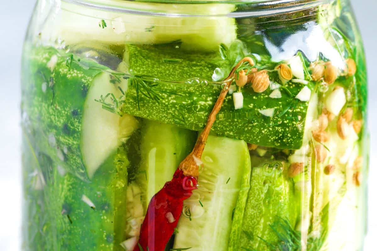 Cucumbers pickling in a brine of vinegar, spices, dill, garlic, and salt.