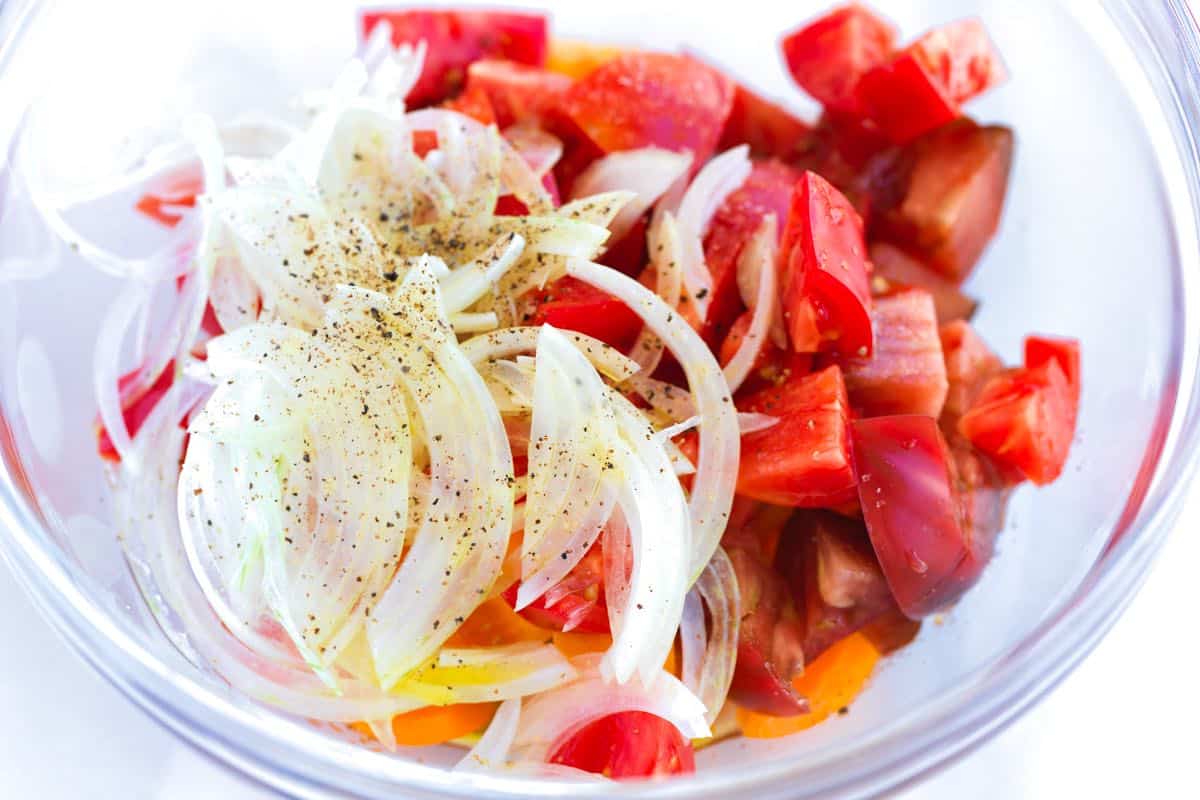 Marinating tomatoes with onions, salt, sugar, vinegar, and olive oil for panzanella salad