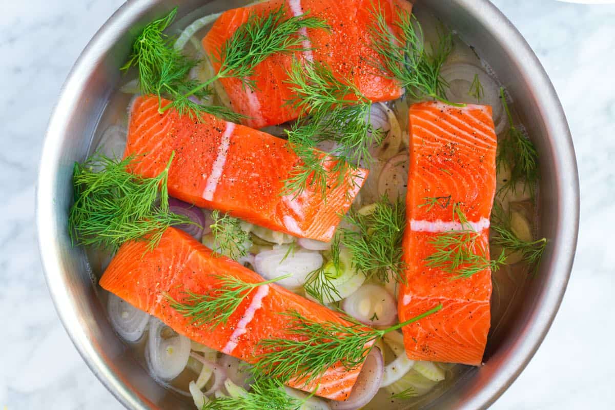 Adding fresh dill to the salmon in the skillet for poached salmon fillets