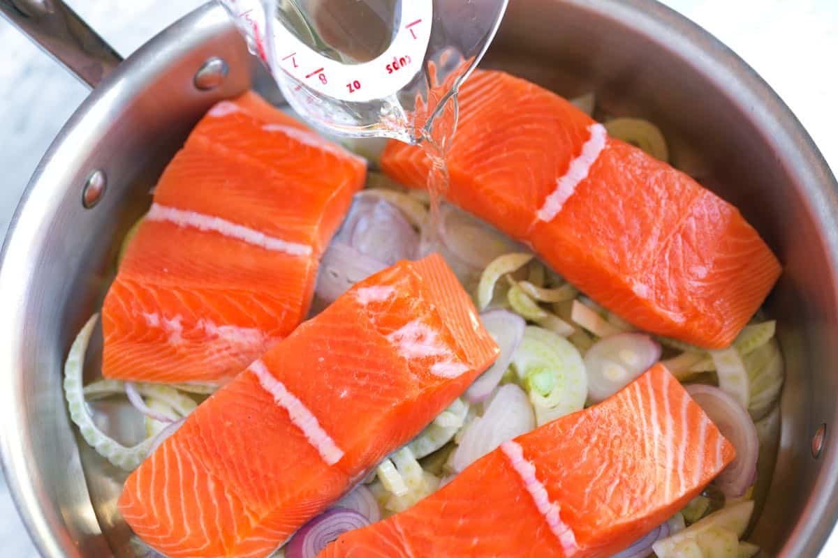 Pouring wine and water into the skillet for poached salmon