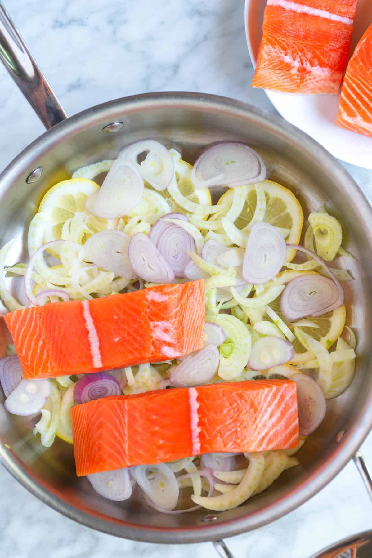 Skillet with lemon slices, shallot, fennel and salmon fillets almost ready for poaching