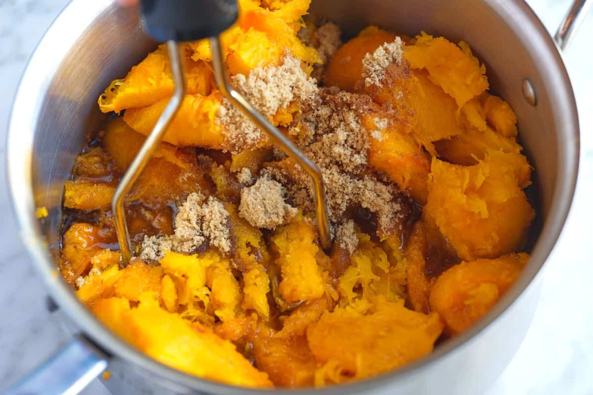 Mashing roasted pumpkin, maple syrup, brown sugar, and spices together in a saucepan