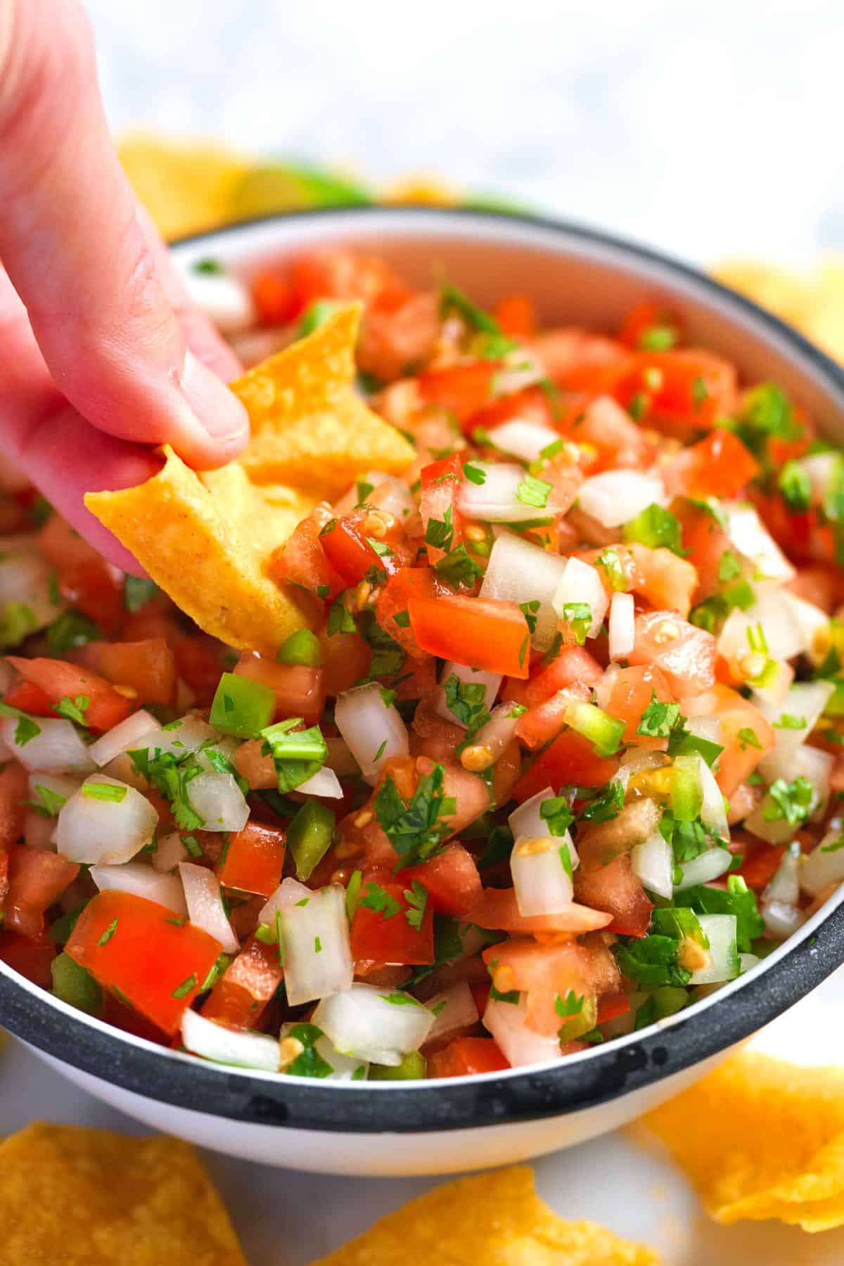 Scooping homemade pico de gallo with a tortilla chip.