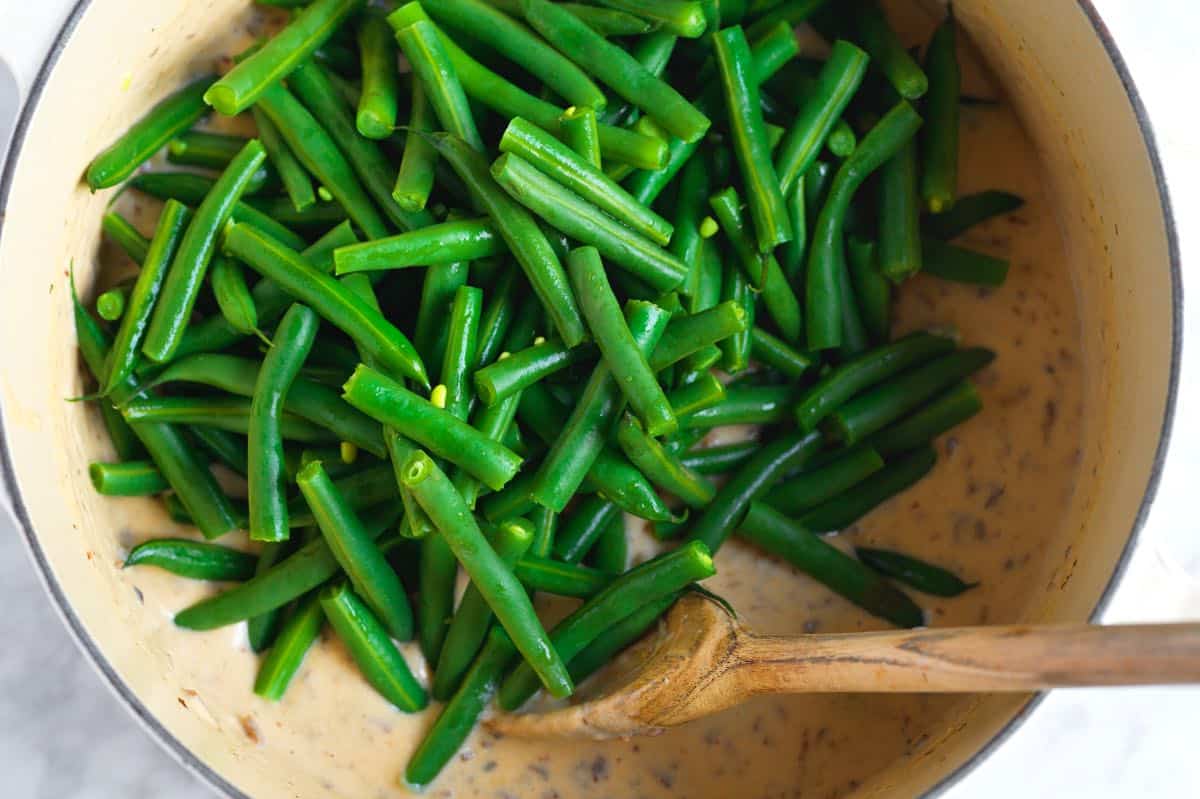 Stirring the blanched green beans into the creamy casserole sauce.