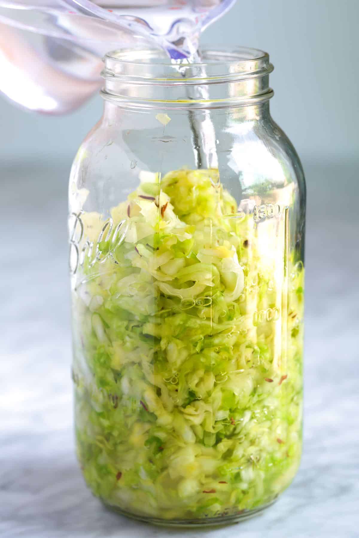 Pouring a 2% salt brine into a jar with cabbage for fermented sauerkraut