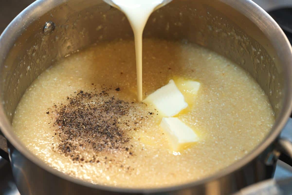 How to make grits: Adding butter, cream, salt, and pepper to the grits on the stove.