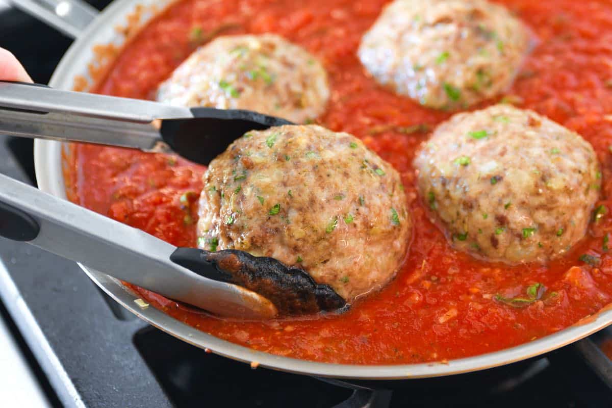 Placing partially cooked meatballs into homemade tomato sauce.