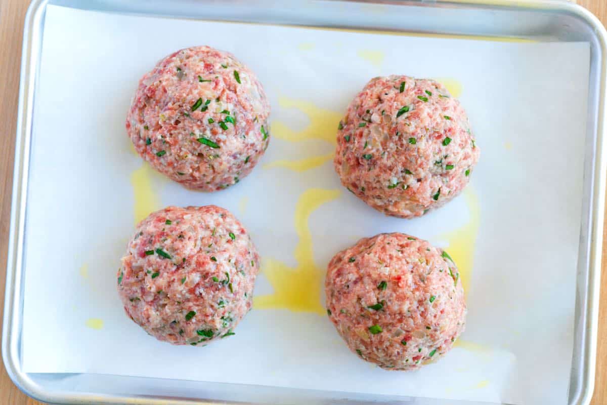 Four big Italian meatballs on a baking sheet ready to go into the oven.