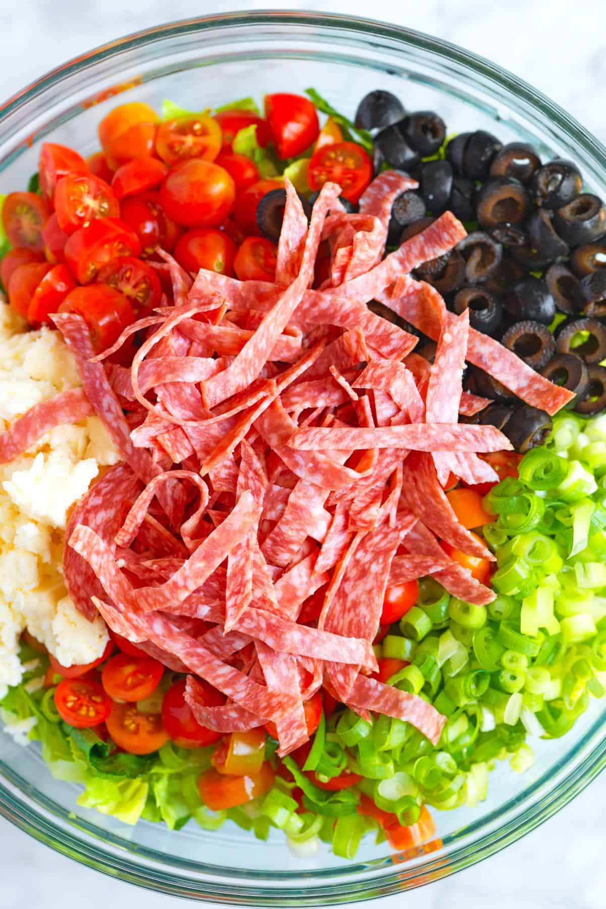 Chopped Salad Ingredients in a bowl (romaine lettuce, salami, olives, tomatoes, and cheese).