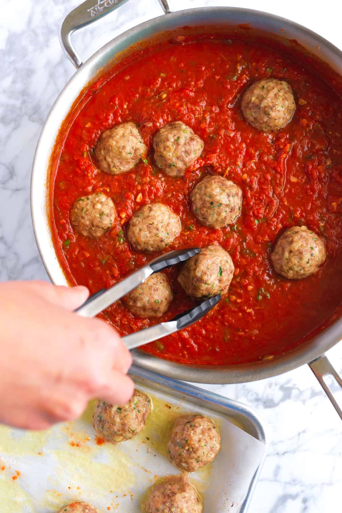 Putting baked meatballs into homemade marinara sauce ready for spaghetti and meatballs