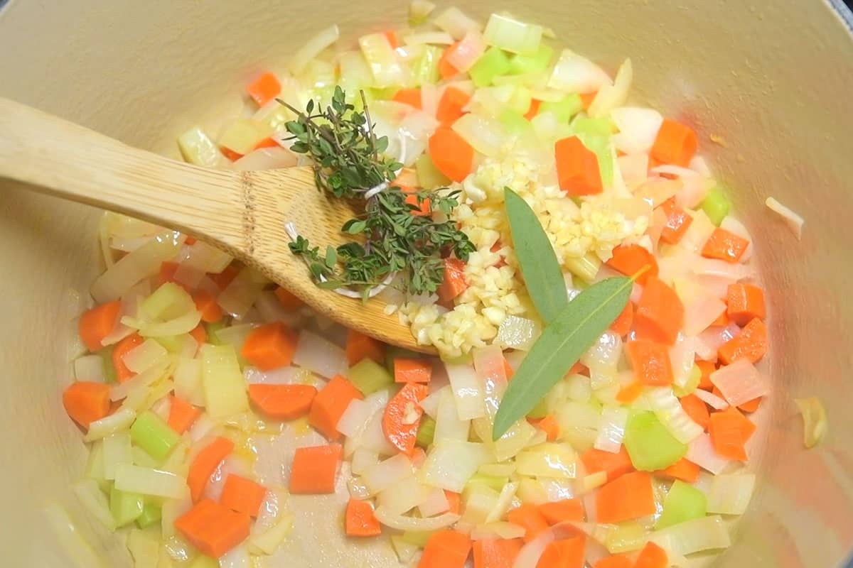 Step for making chicken noodle soup - cooking onion, carrot and celery in a pot