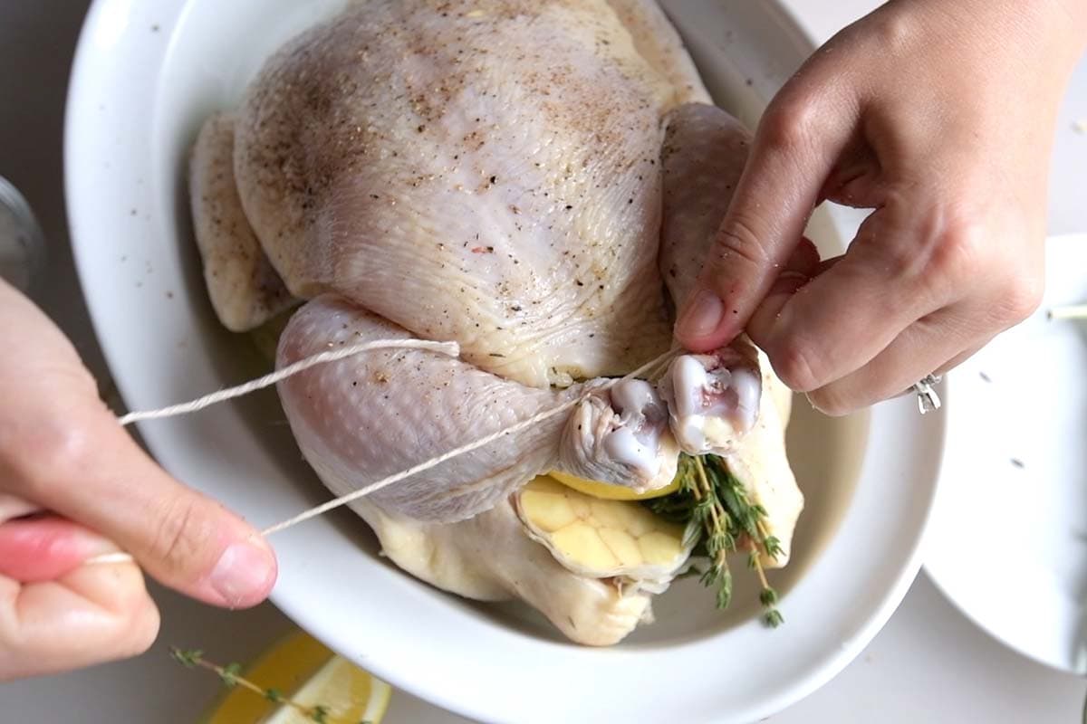 Seasoning whole chicken and trussing the legs in preparation for roast chicken